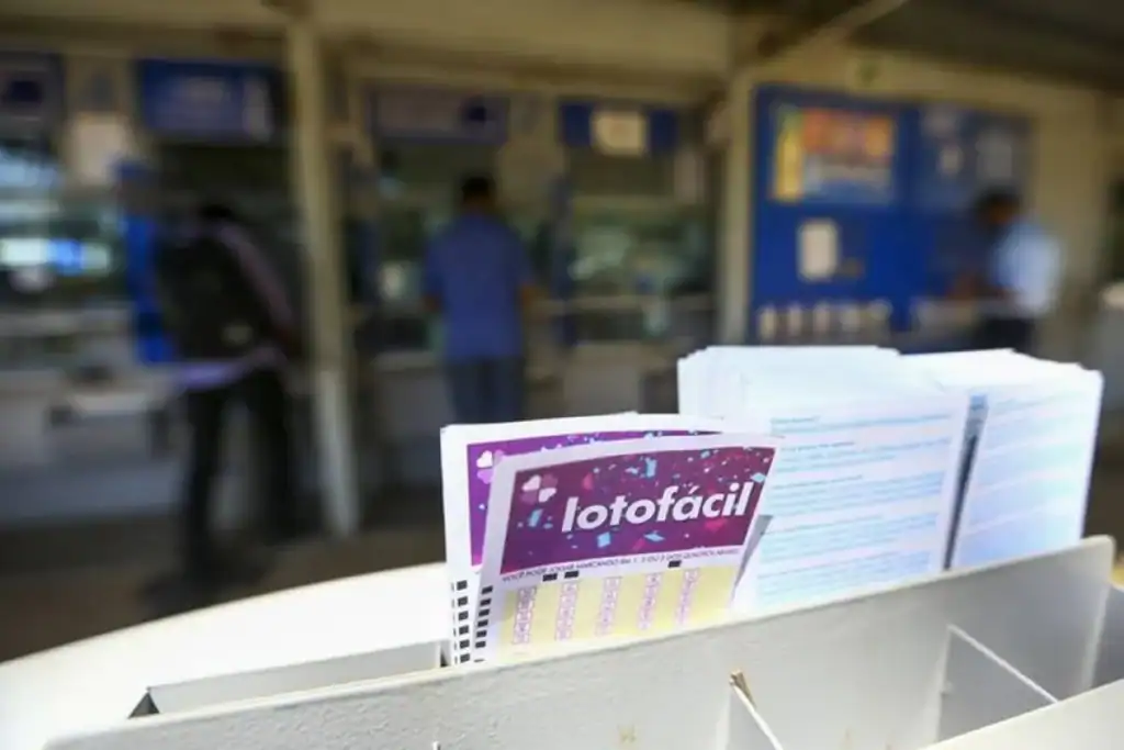 Loterias Lotofácil sorteia milhões hoje: Confira resultados Mão segurando um bilhete da Lotofácil após o sorteio, com dinheiro ao fundo, representando que Loterias Lotofácil sorteia milhões hoje.